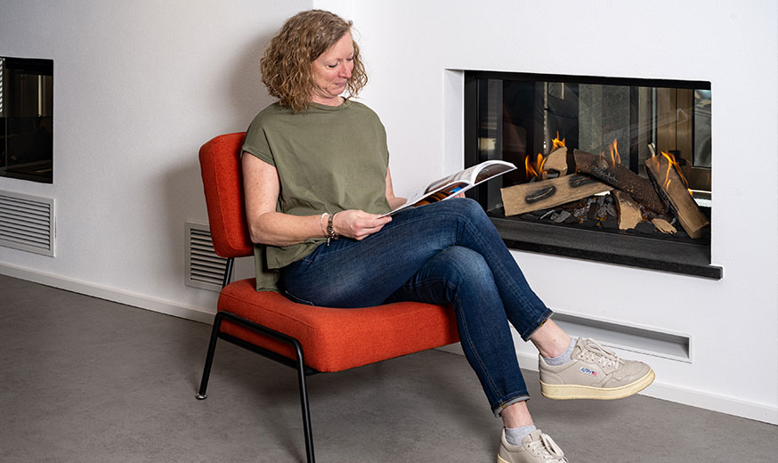Frau mit Prospekt auf einem Sessel vor einem Kamin im Mac Metzler Showroom in Katzenelnbogen